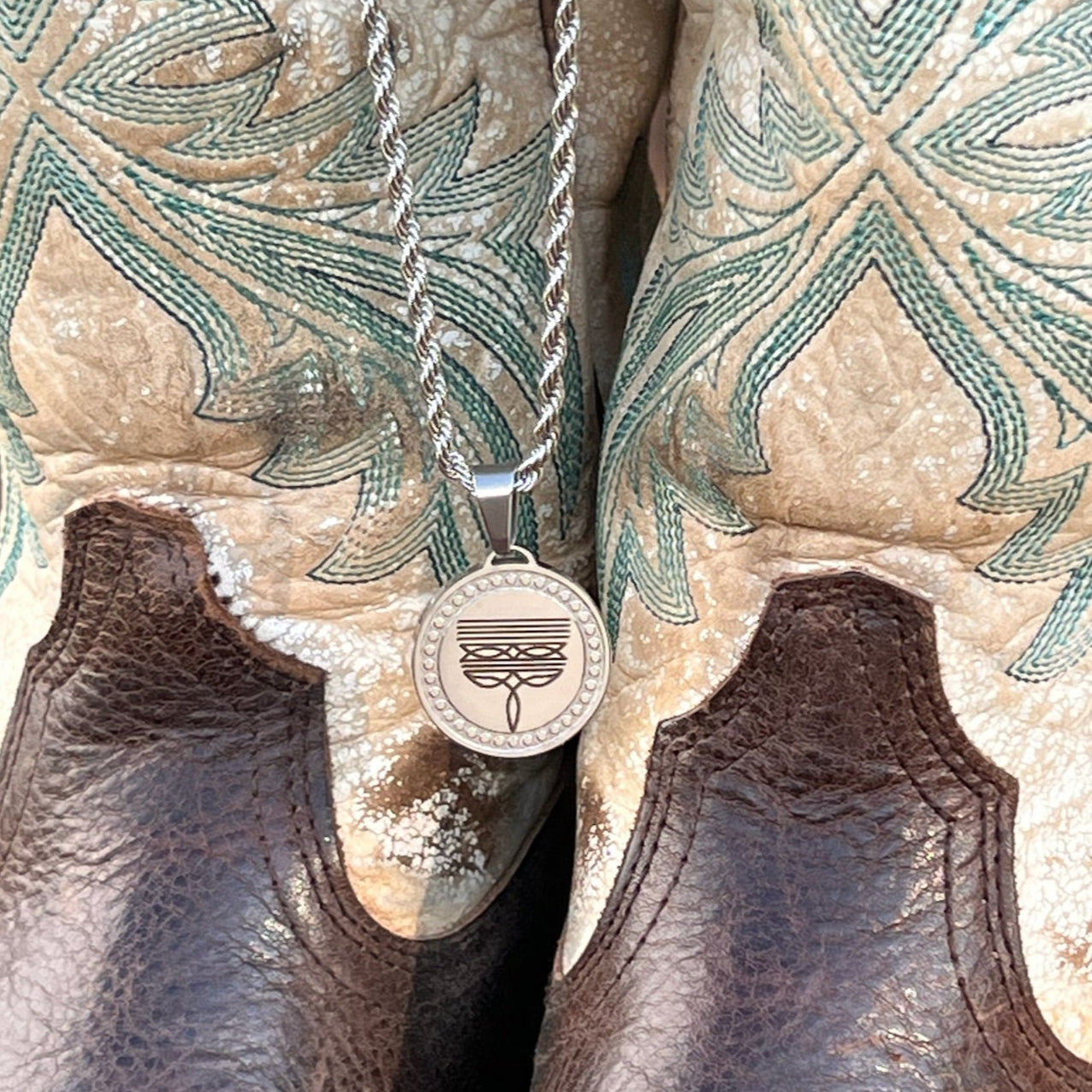 Silver necklace with a pendant on a pair of brown leather boots with intricate patterns.